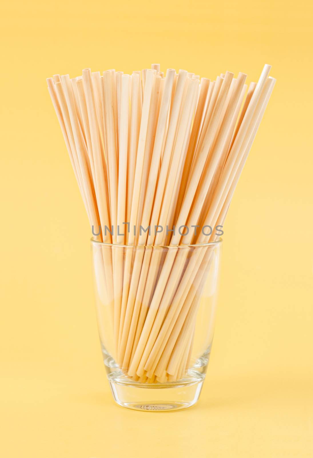 Wheat Straws for drinking water natural eco friendly renewable in glass on yellow background.