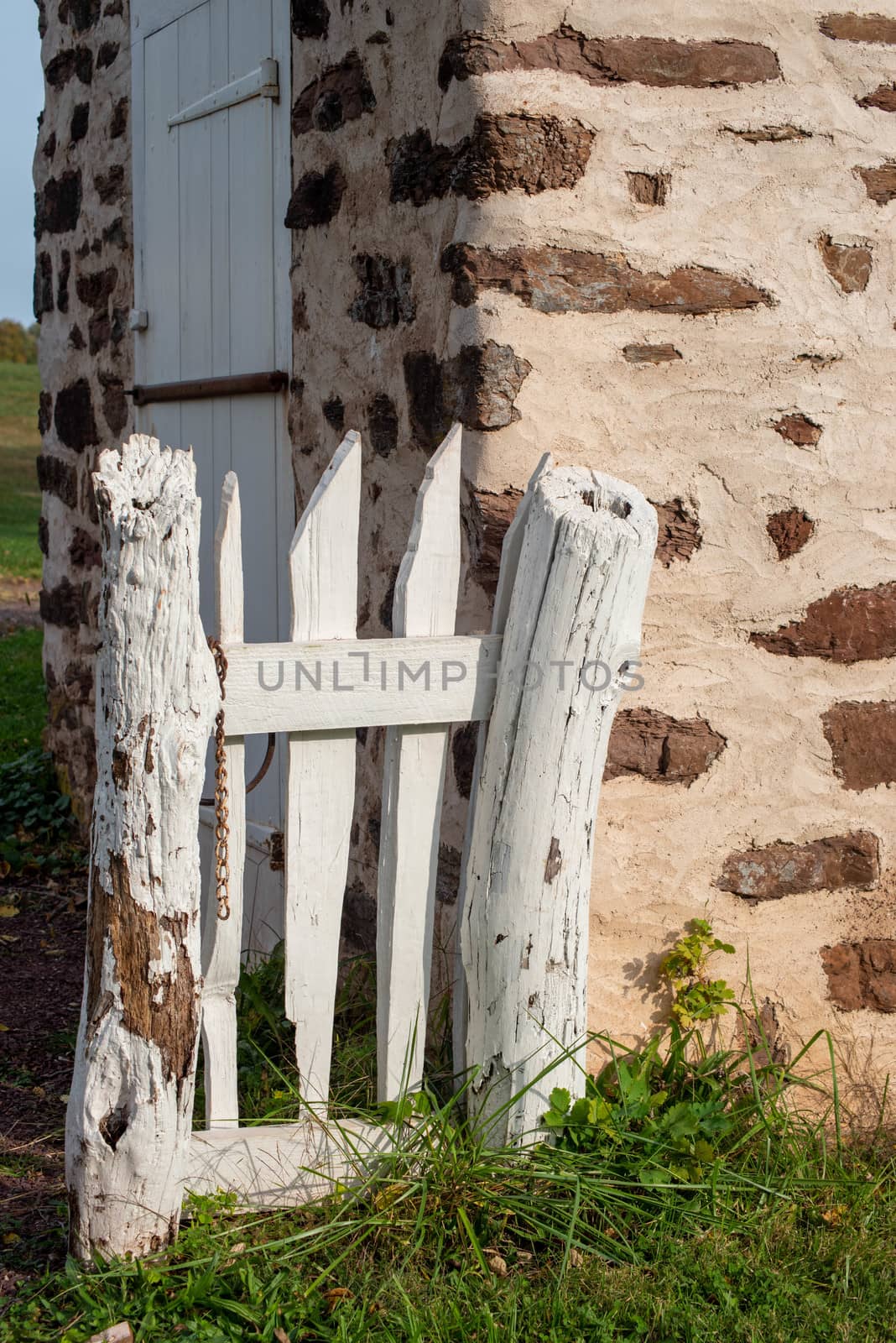 Beautiful cozy scene of a rustic white wooden gate by a stone building, with green grass and copy space