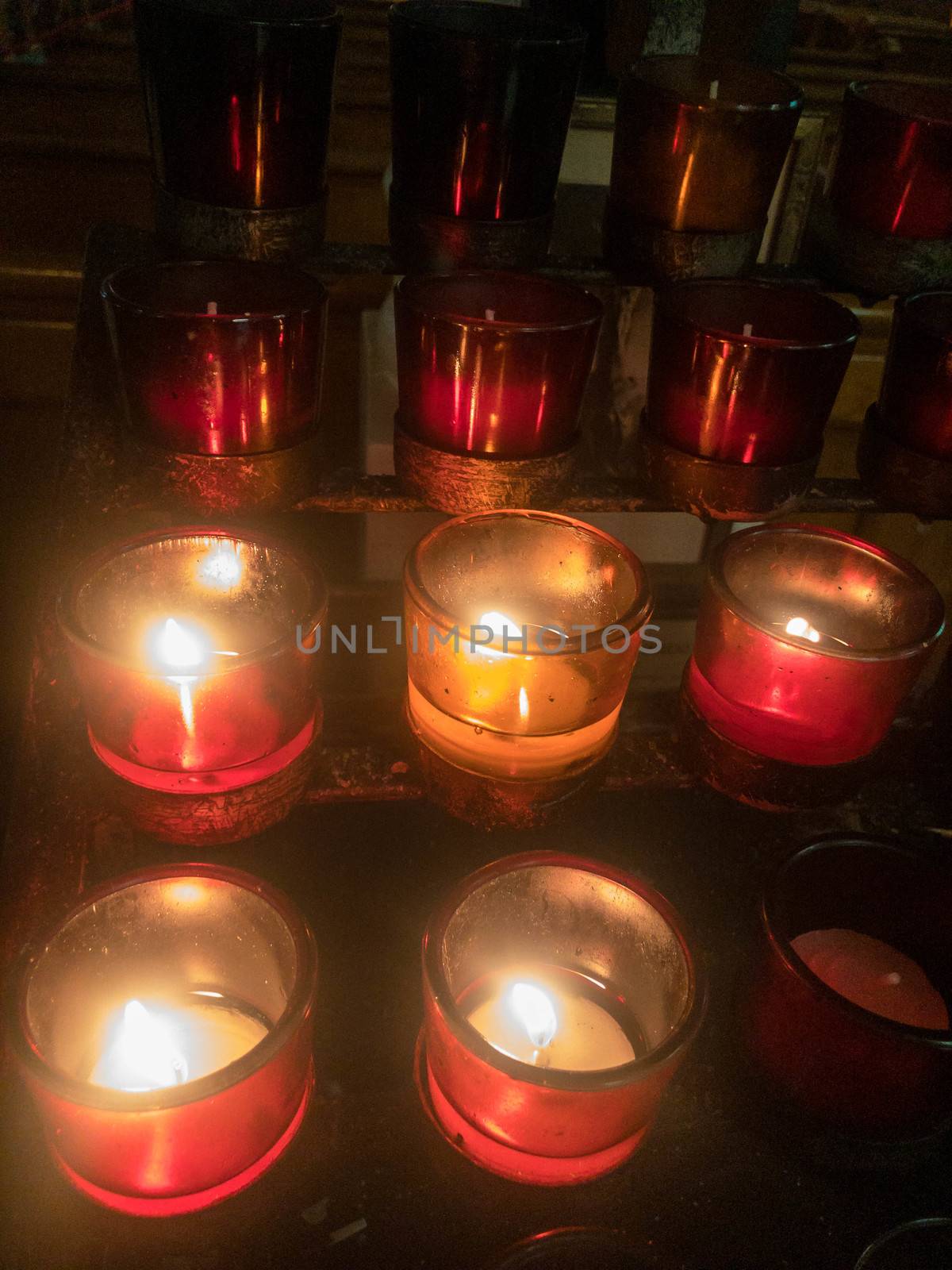 Tiered rows of tiny votive candles flicker and glow in a dark church.