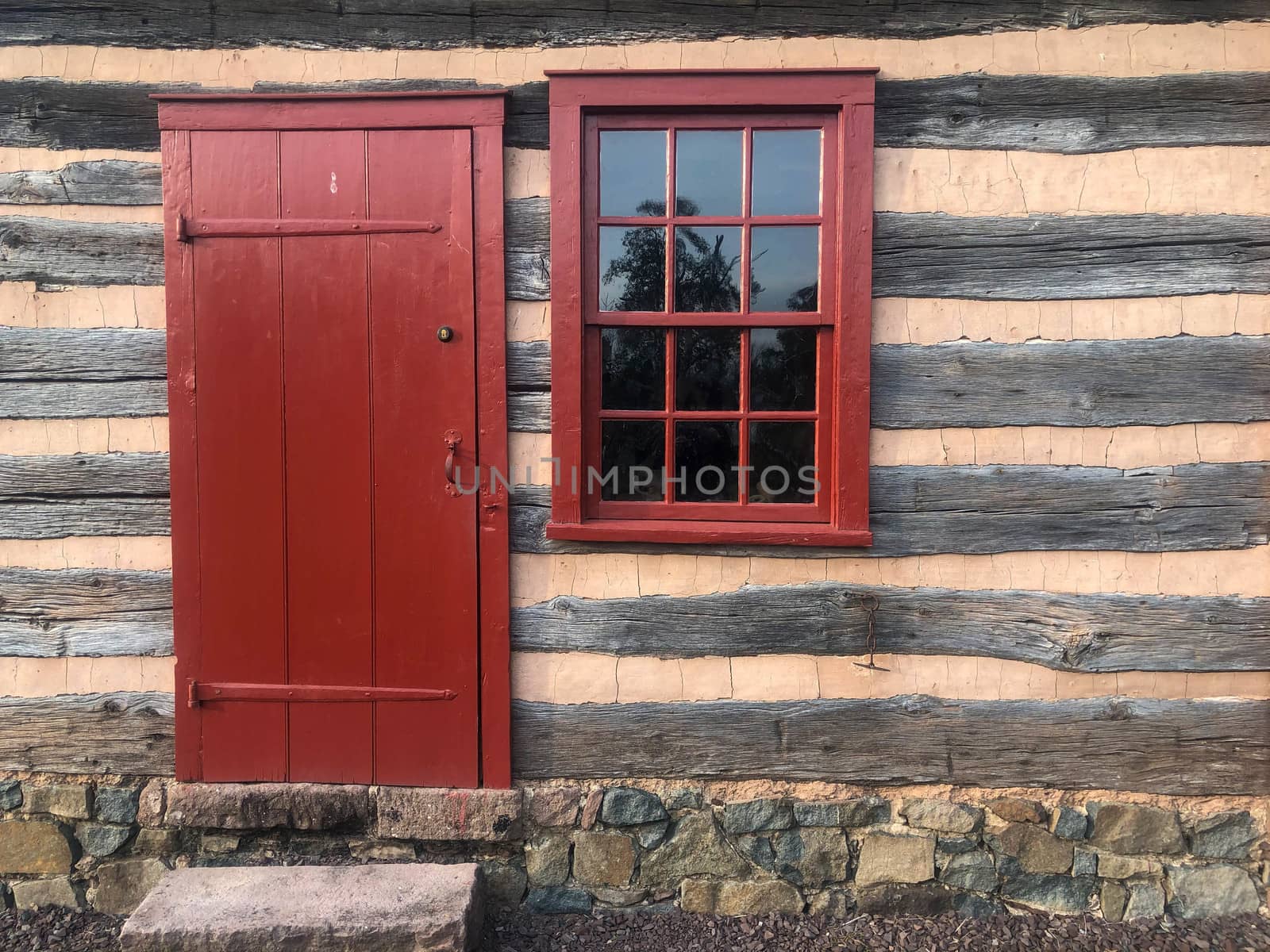 Red door and 12-pane window in colonial American log cabin by marysalen