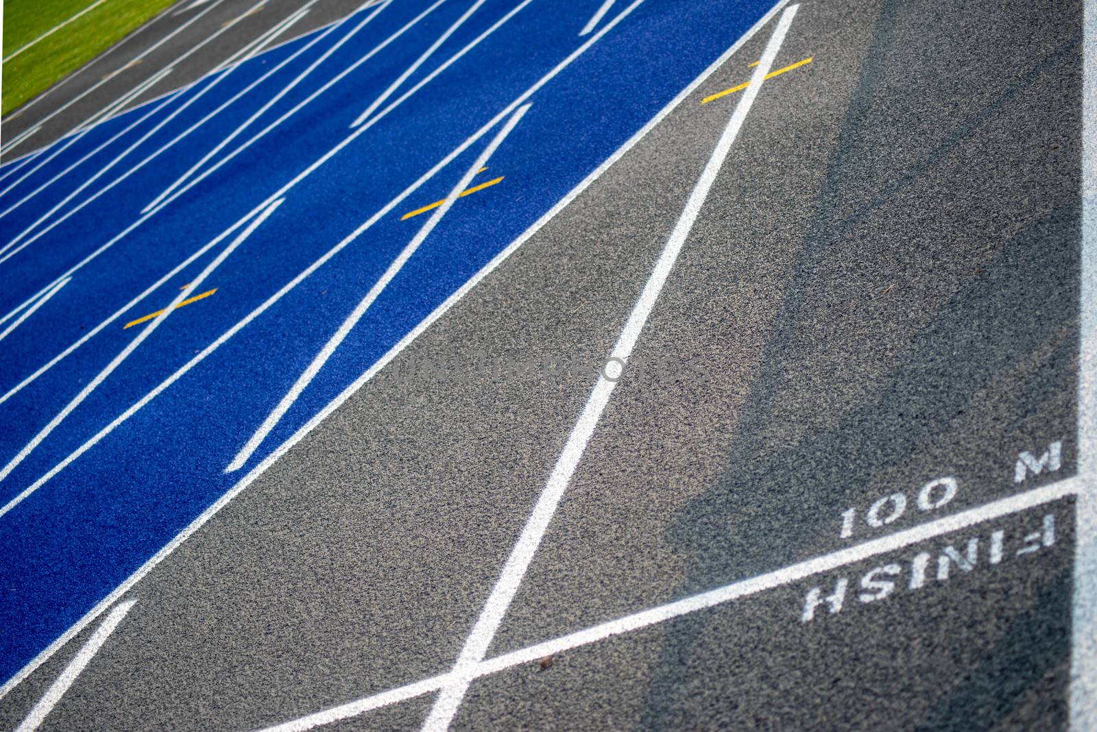 Full frame image in natural light of textured surface of a clean, new outdoor blue and gray running track with crisp fresh white lines and copy space. Green grass in the background.