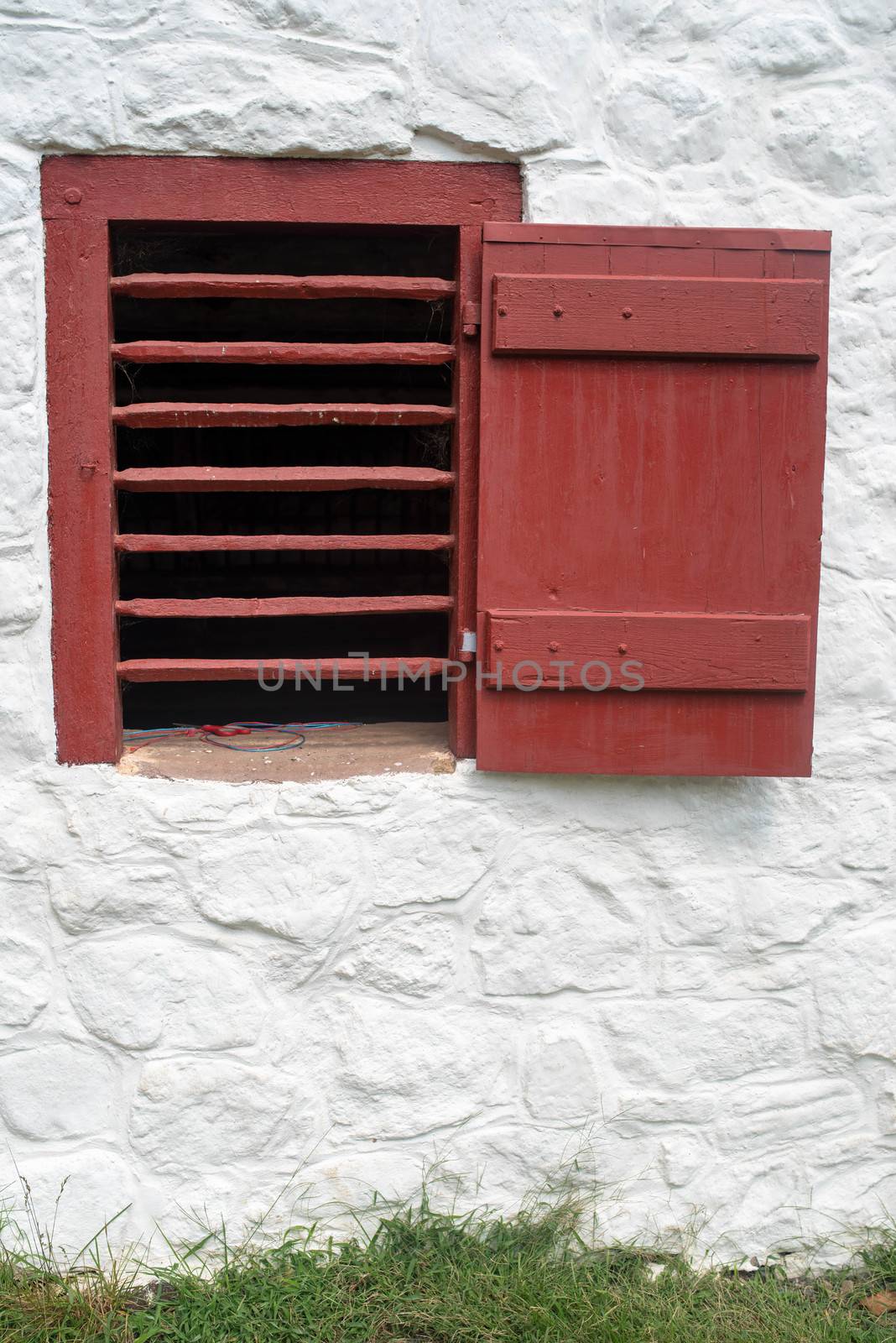 Whitewashed  stone barn with red slatted ventilation window and open shutter in a grassy field. Rustic charm and beauty in natural light with copy space.