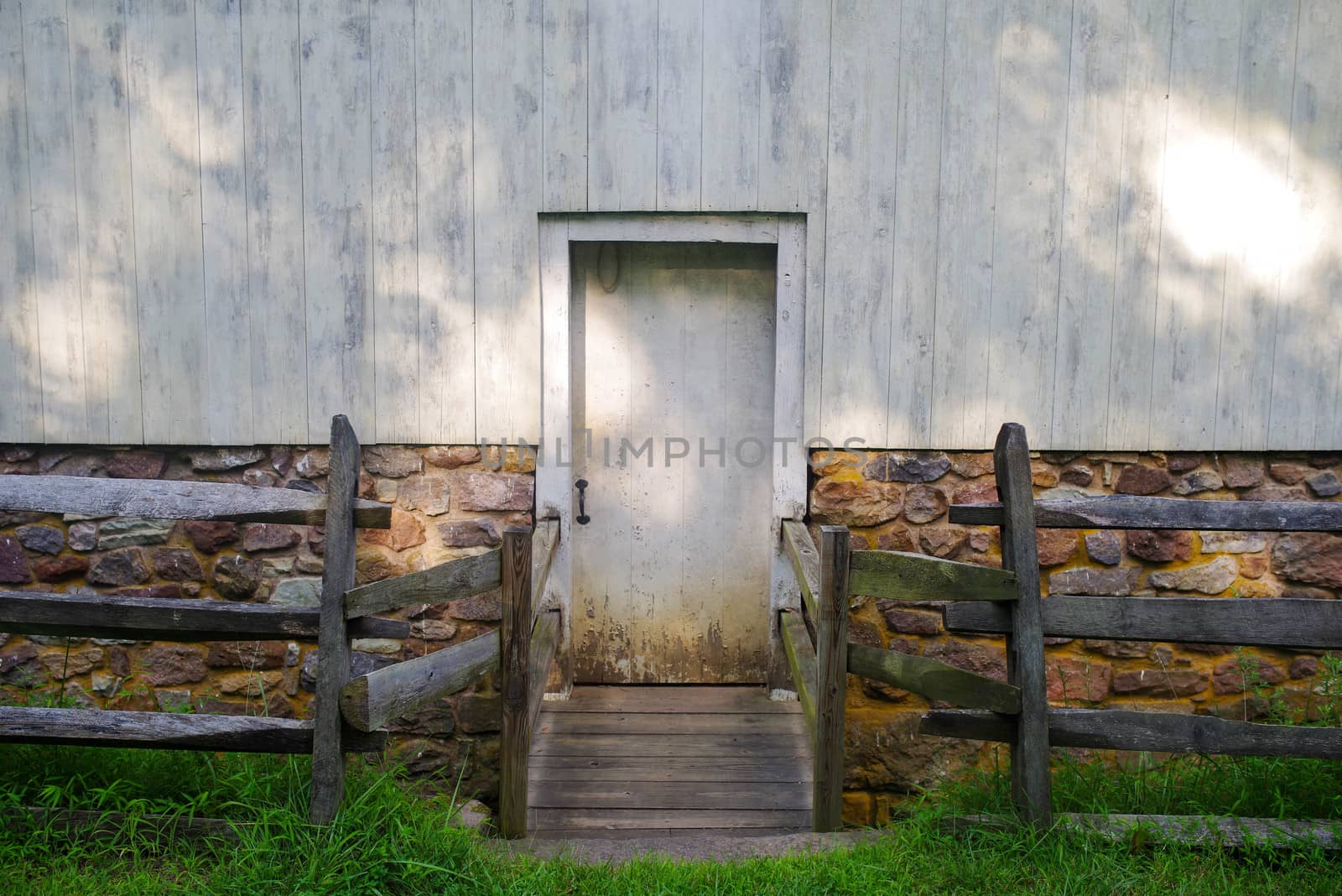 Recessed door sits back  from green grass and wooden fence, centered in dappled golden hour sunlight.