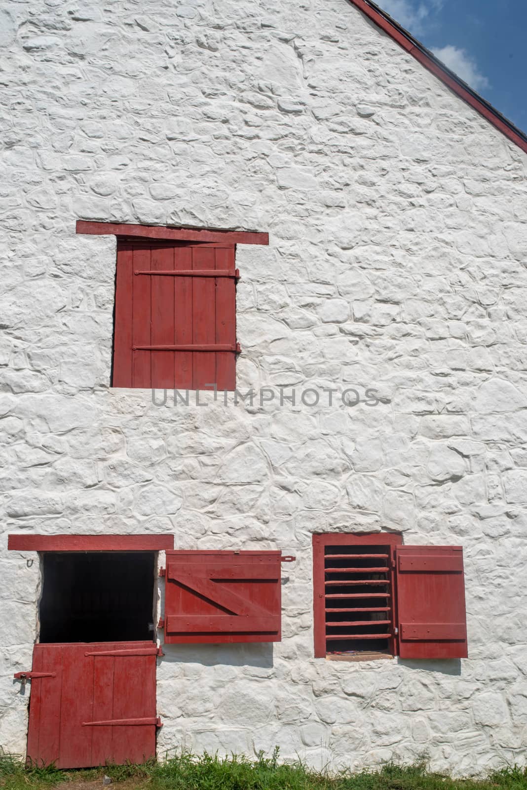 Full frame in natural light with copy space. Image shows red door, shutters, and slatted window on a whitewashed stone wall.