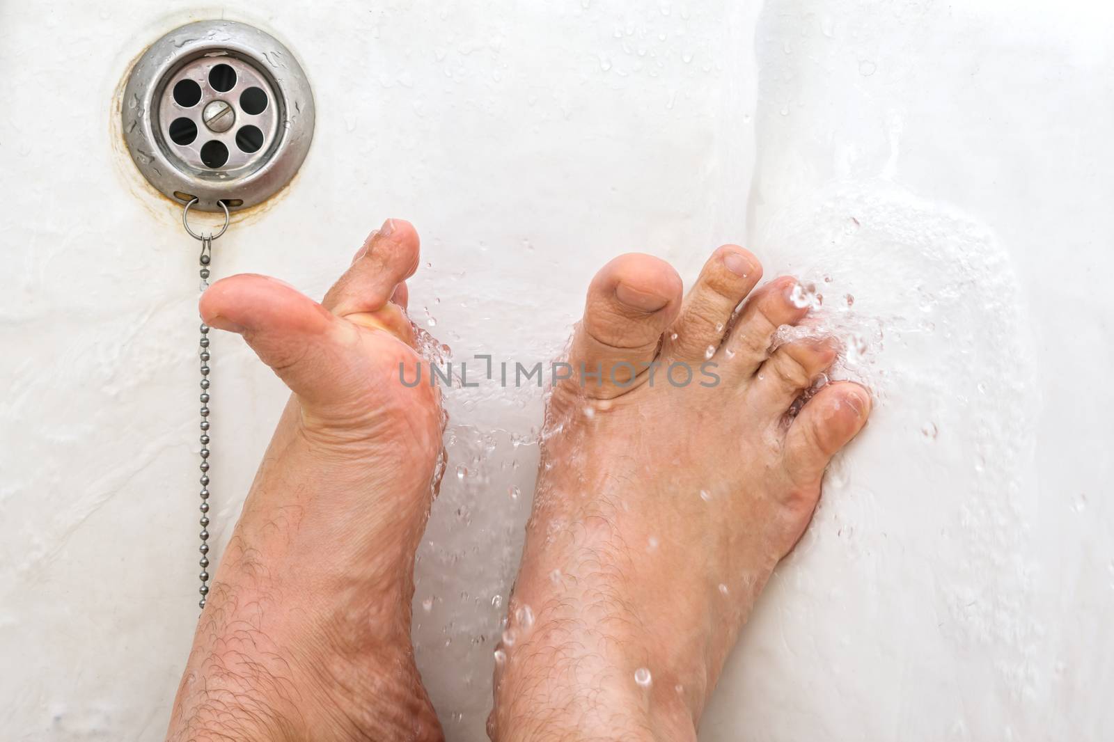 Washing feet in running water while lying in a bathroom close-up