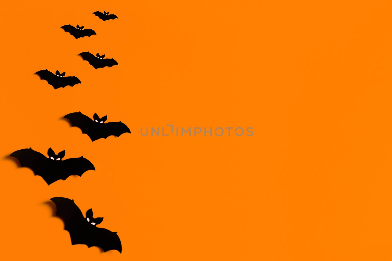 orange background with a flock of black paper bats for Halloween, black paper bat silhouettes on an orange background, Halloween concept, copyspace, flatlay, top view, overhead by Pirlik