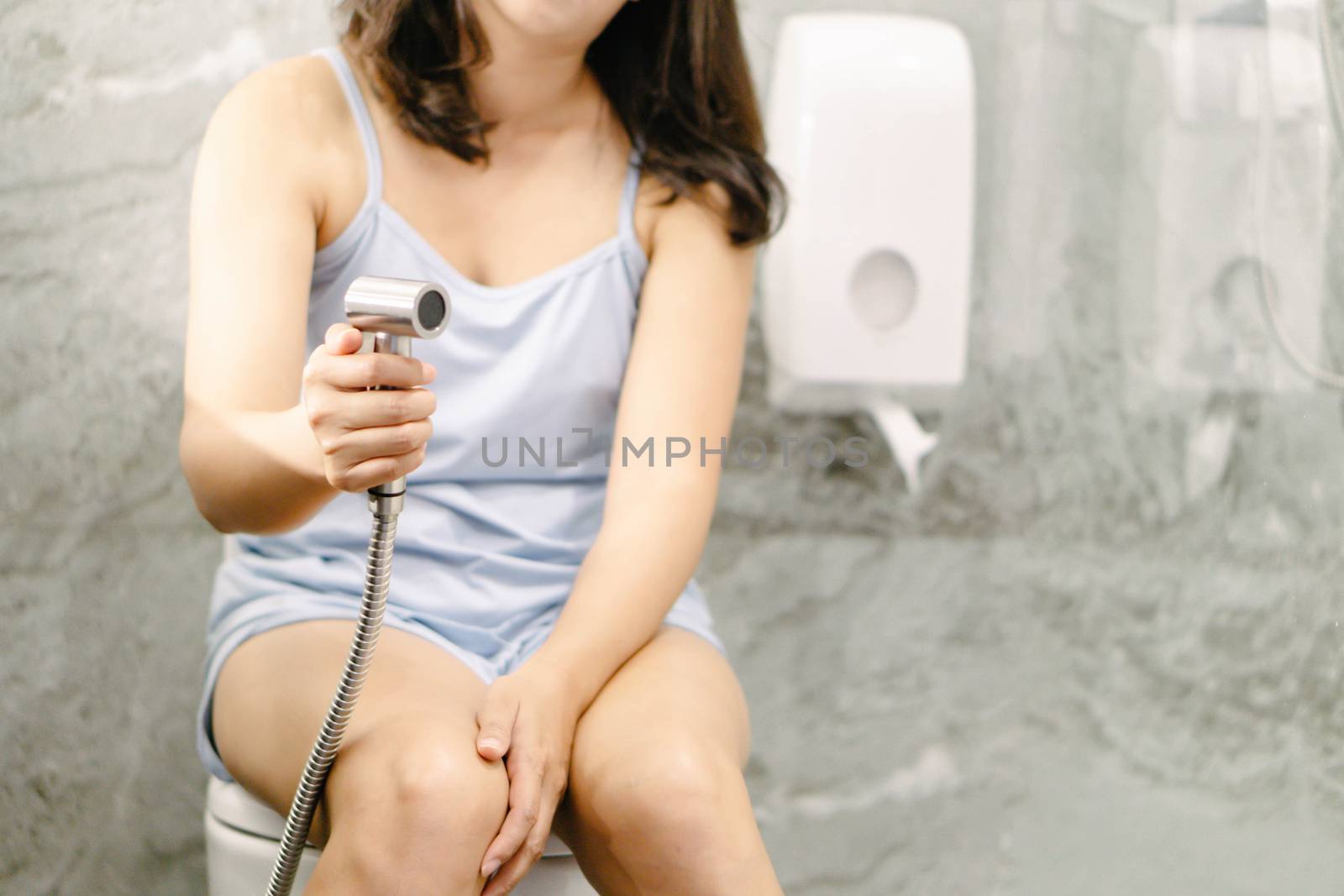 Woman hand using Chromium bidet shower sitting on toilet