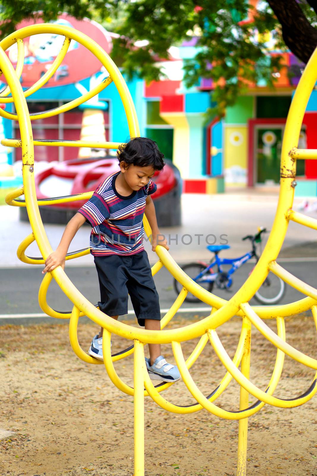 An Asian boy is climbing on a playground equipment in a school.