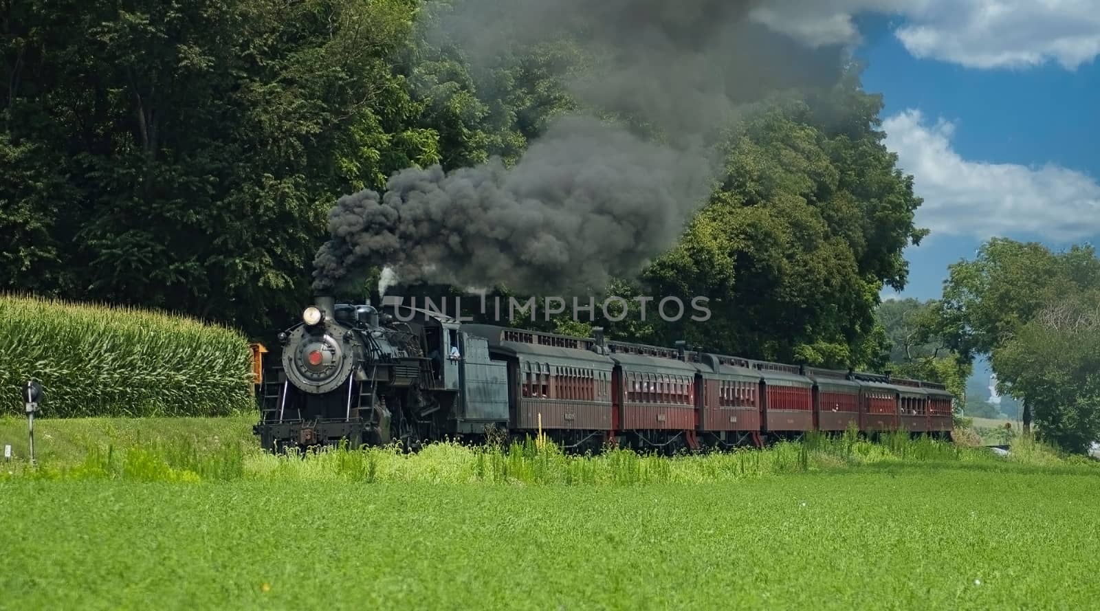 Antique Steam Passenger Train Puffing along Amish Countryside with Green Fields