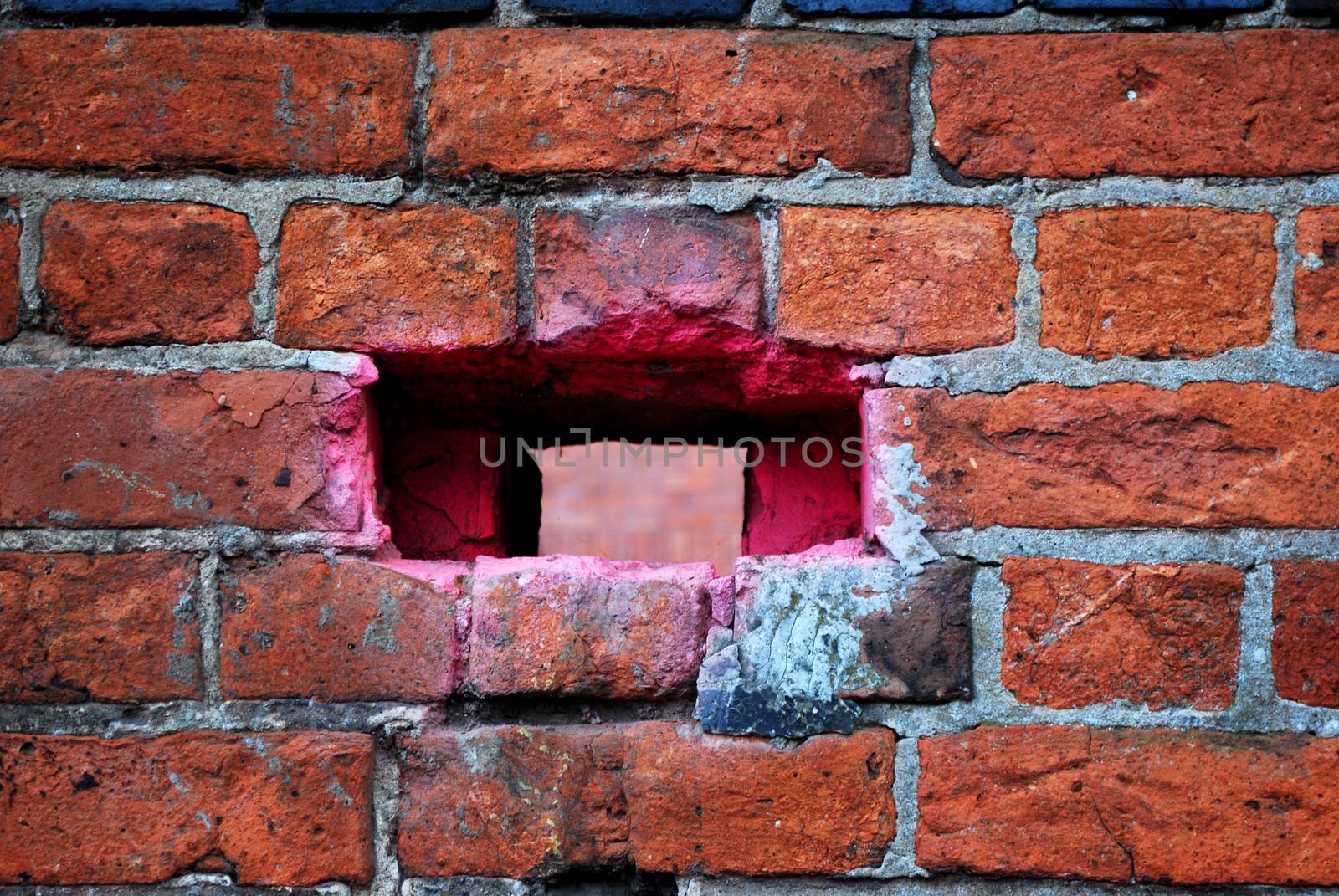 A hole in a brick wall that has been spray painted pink