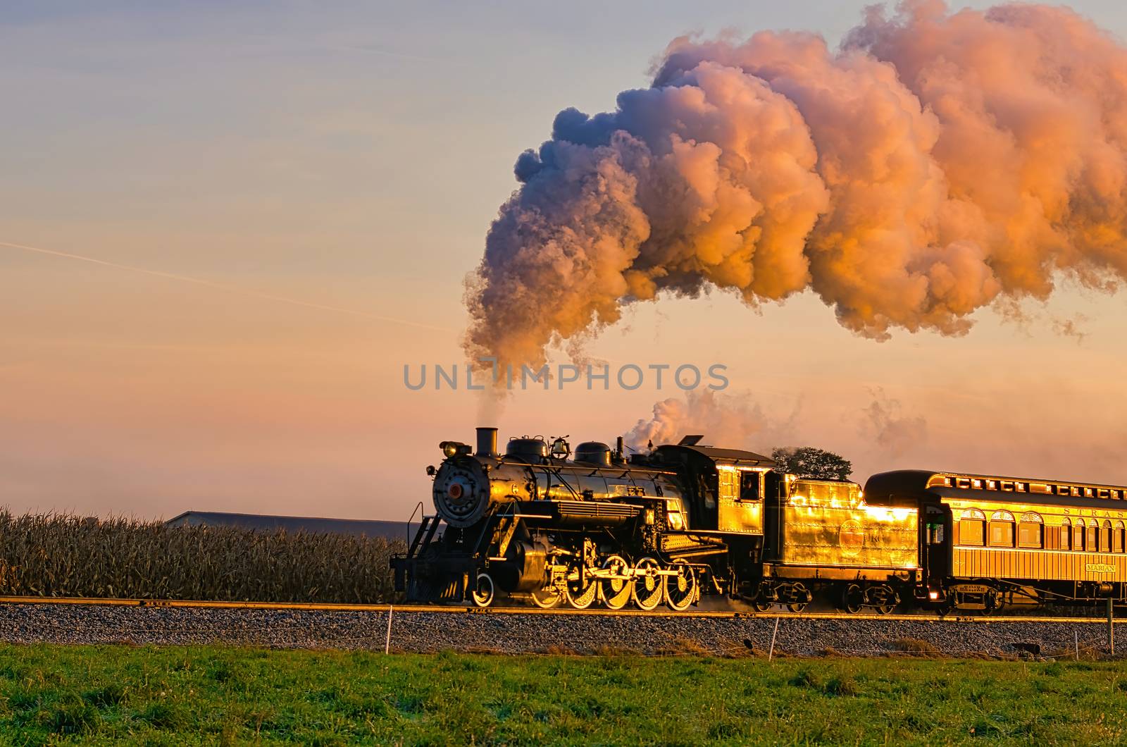 View of Golden Steam Passenger Train at Sunrise Traveling Thru Amish Countryside with lots of Smoke and Steam