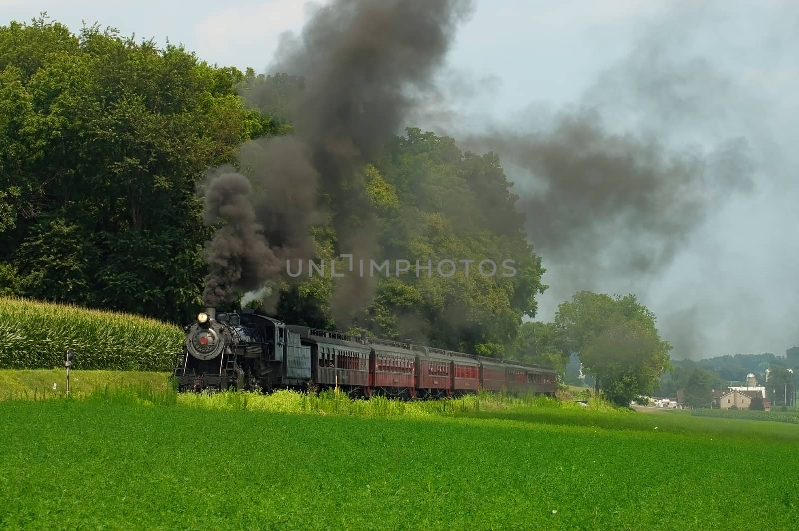 Antique Steam Passenger Train Puffing Lots of Black Smoke along Amish Countryside with Green Fields