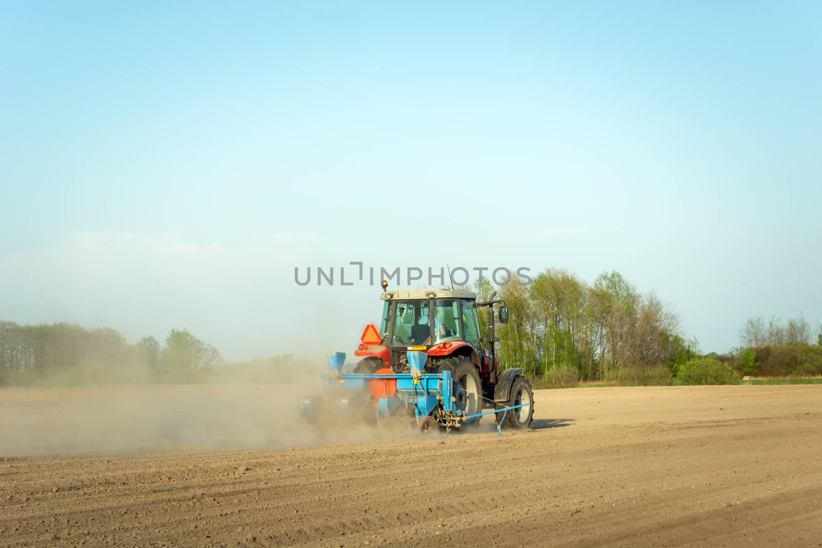 Tractor ploughing the field, dust from dry soil, spring agricultural work