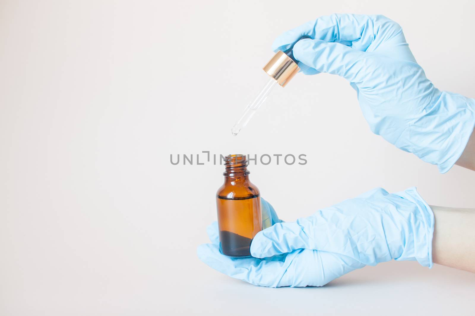 Bottles with serum for the face in his hands in protective medical rubber gloves on a light background. by malyshkamju