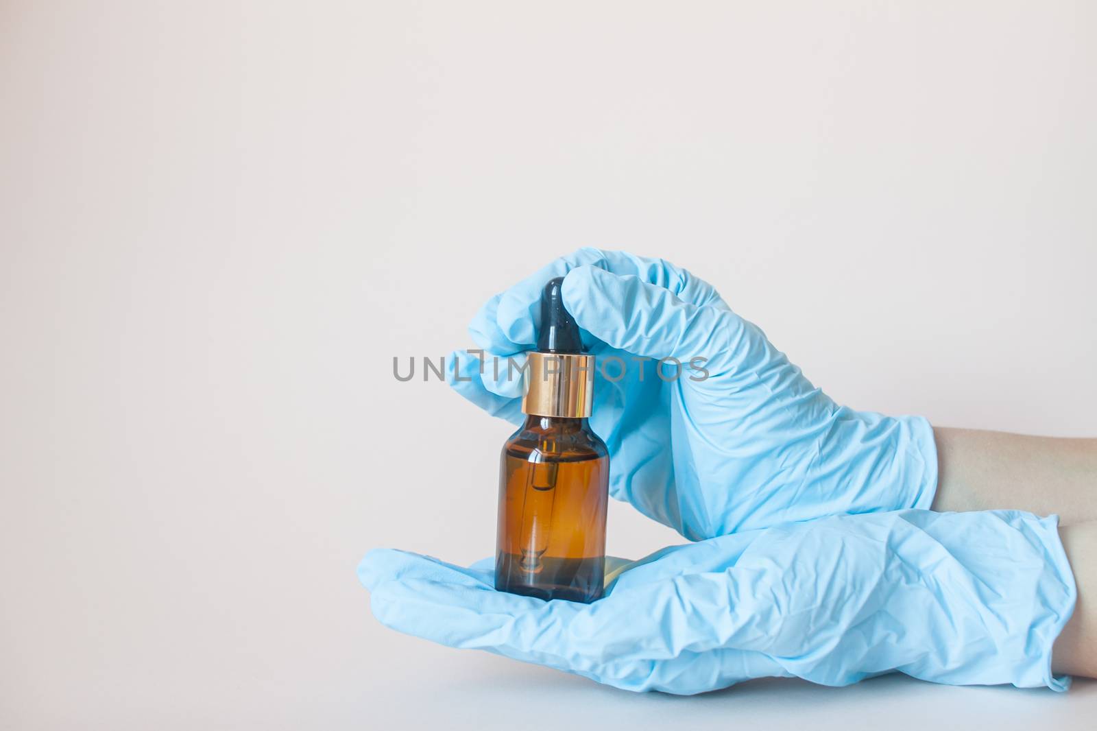 Bottles with serum for the face in his hands in protective medical rubber gloves on a light background. Beauty industry.