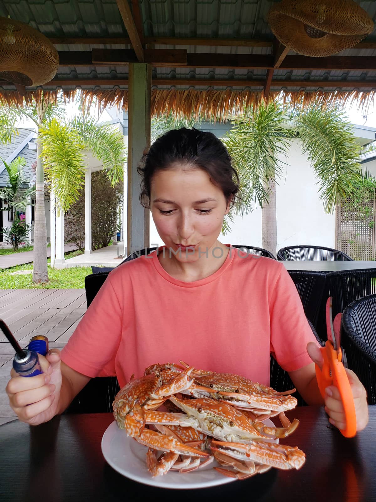 The girl is going to eat boiled crabs. The girl at the table with a full plate of boiled blue crabs.