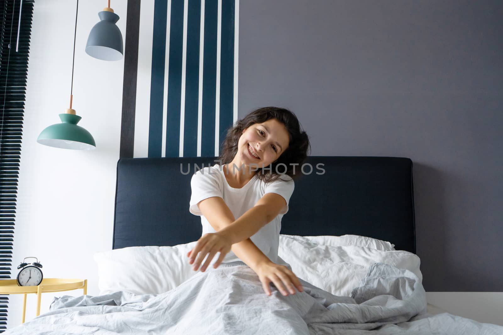 Beautiful girl wakes up in a good mood in a stylish apartment. Stretches with a smile starting the day.