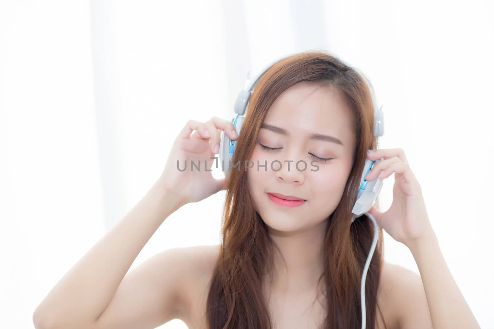 Beautiful asian young woman enjoy listen music with headphone while sitting in bedroom, relax girl with earphone internet online, leisure and technology concept.