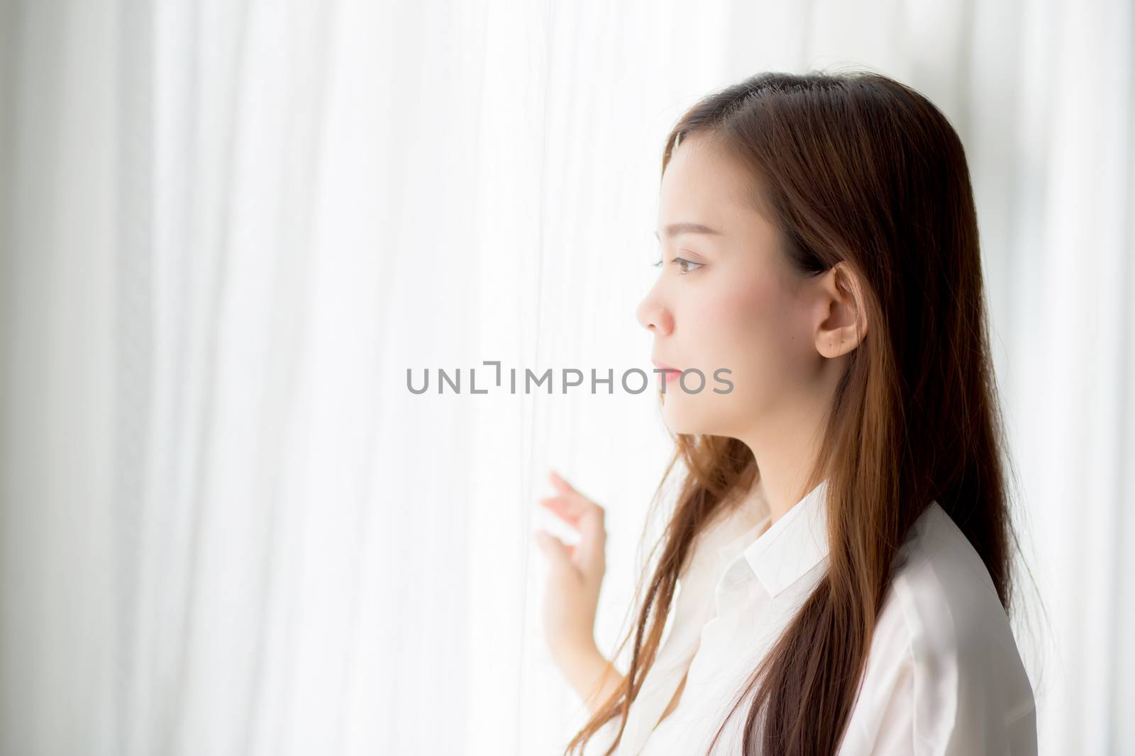 Portrait of beautiful young asian woman standing the window and smile while wake up with sunrise at morning, lifestyle and relax concept.