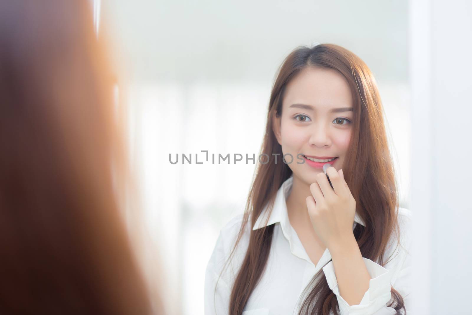 Beauty of portrait of young asian woman at the mirror holding and looking a makeup lipstick, Beautiful girl beauty fashion at the room, lifestyle concept.