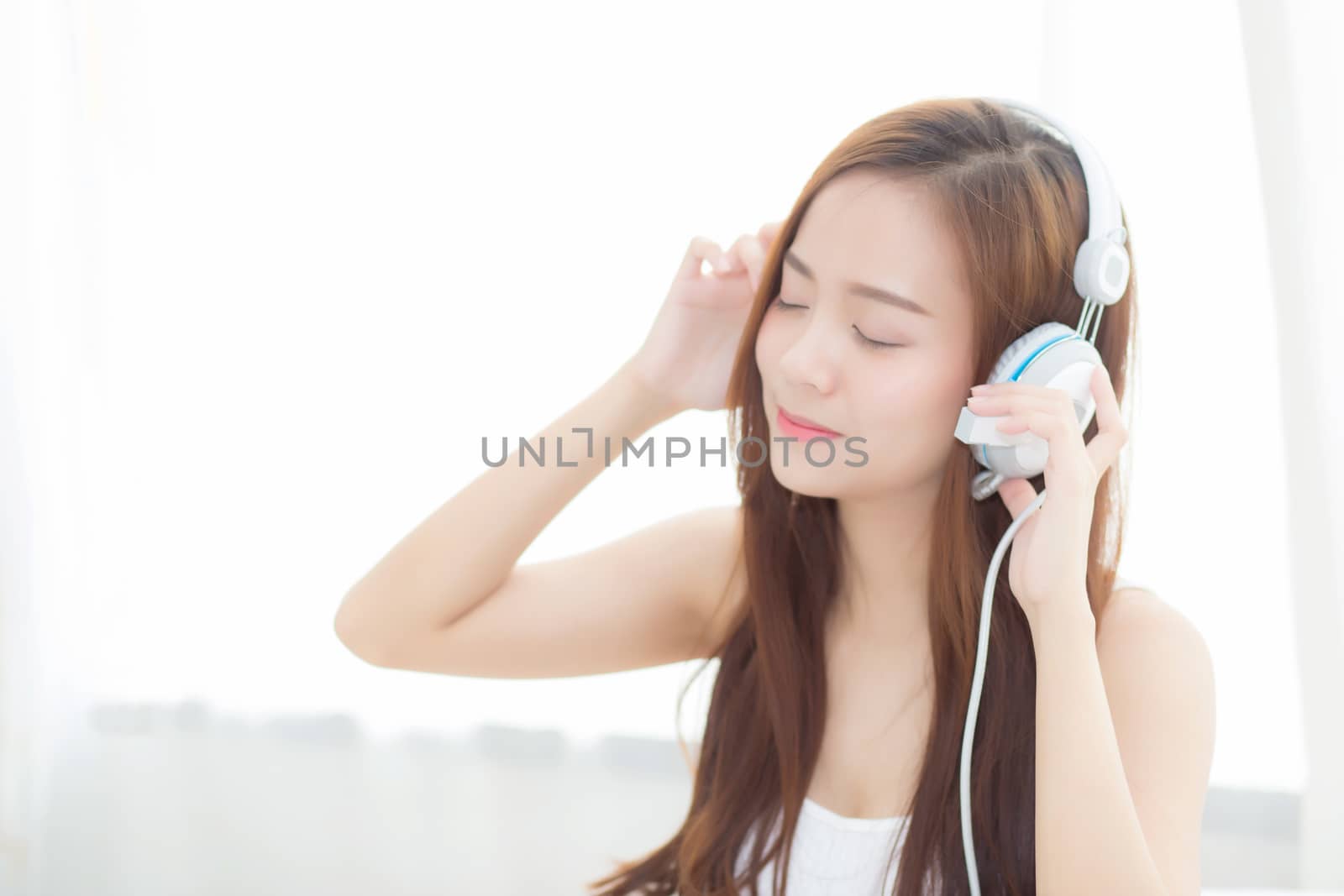 Beautiful asian young woman enjoy listen music with headphone while sitting in bedroom, relax girl with earphone internet online, leisure and technology concept.