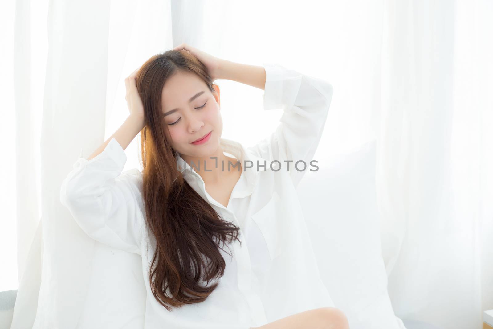 Portrait of beautiful young asian woman standing the window and smile while wake up with sunrise at morning, lifestyle and relax concept.