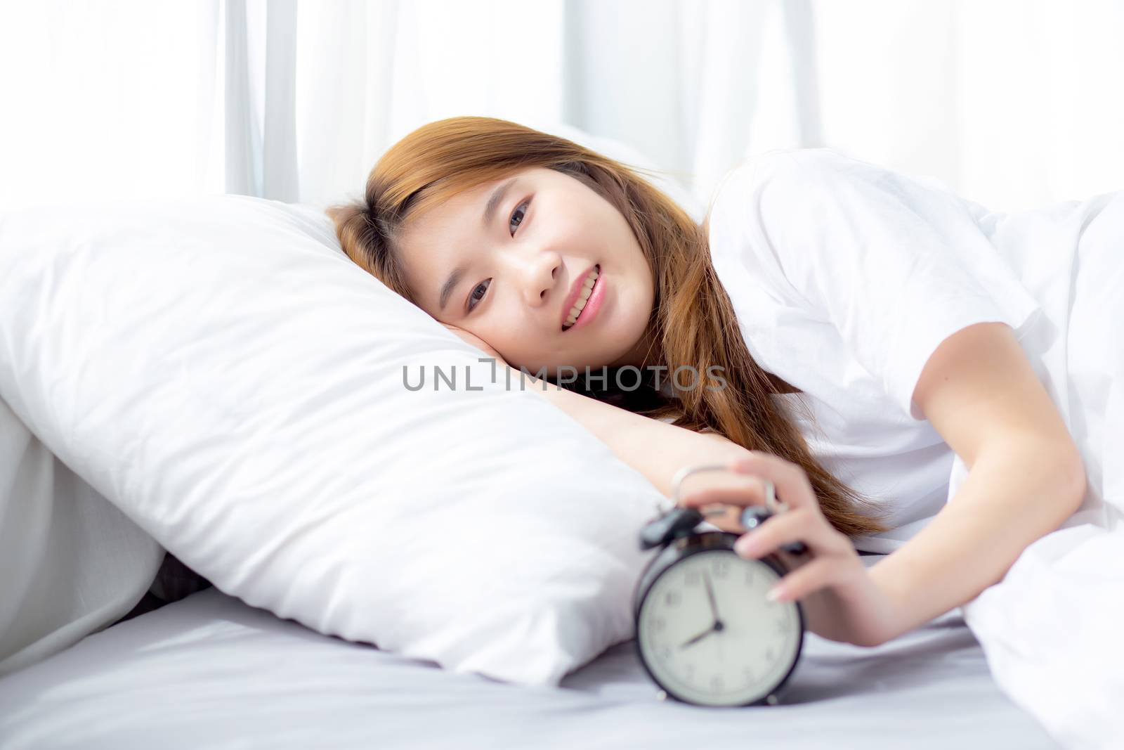 Beautiful of portrait asian young woman turn off alarm clock in morning, wake up for sleep with alarm clock, relax and lifestyle concept.