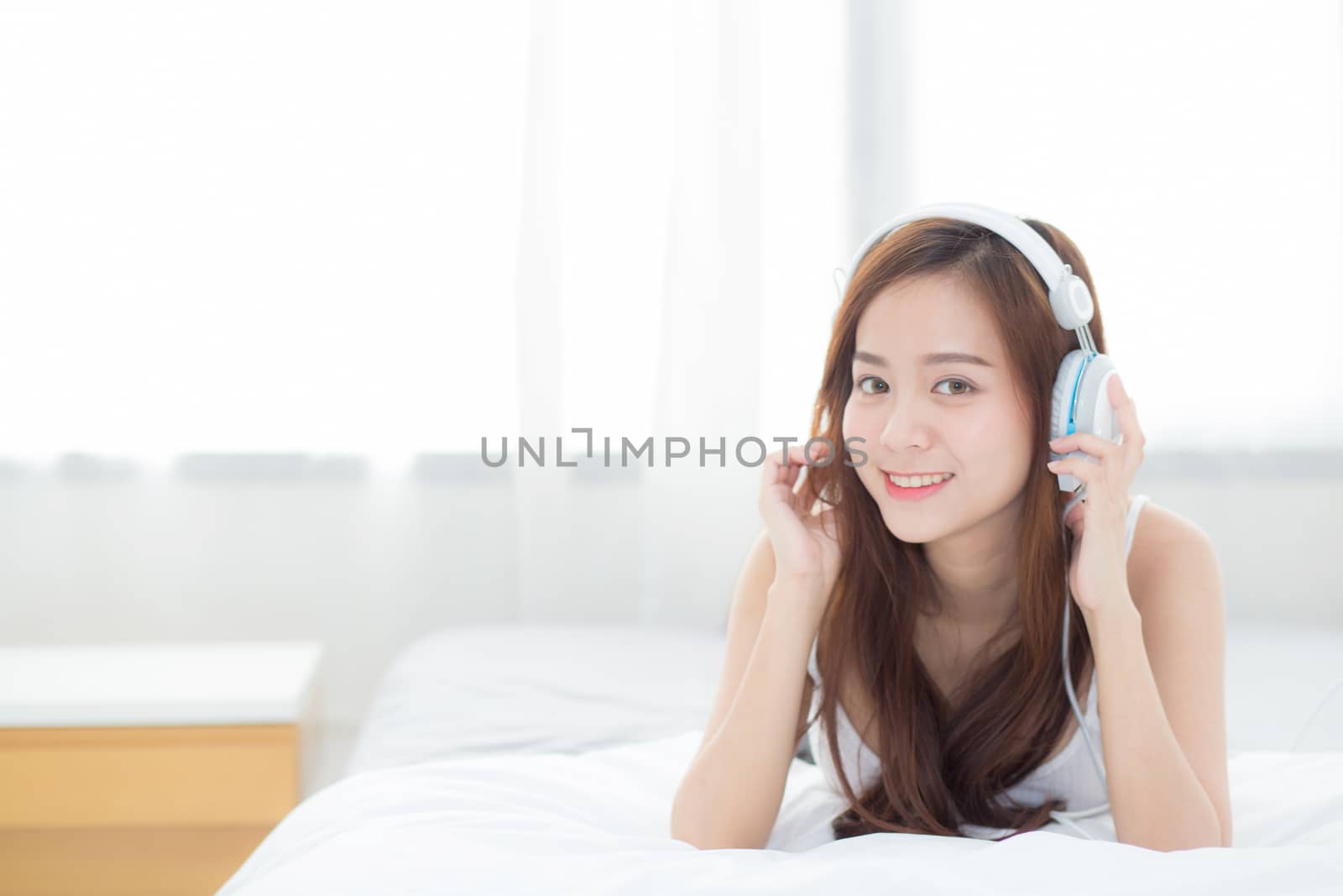 Beautiful asian young woman enjoy listen music with headphone while lying in bedroom, relax girl with earphone internet online, leisure and technology concept.