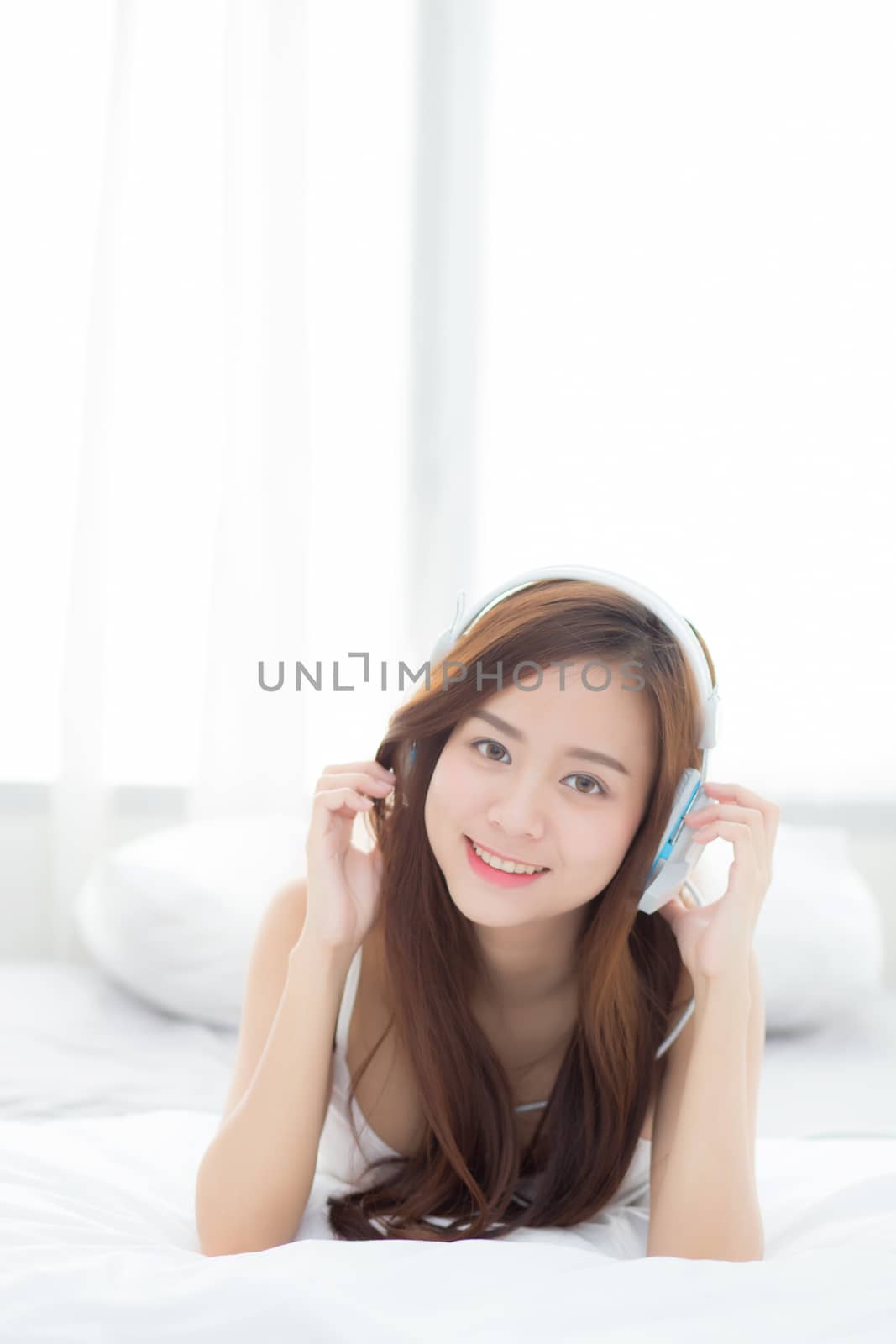 Beautiful asian young woman enjoy listen music with headphone while lying in bedroom, relax girl with earphone internet online, leisure and technology concept.