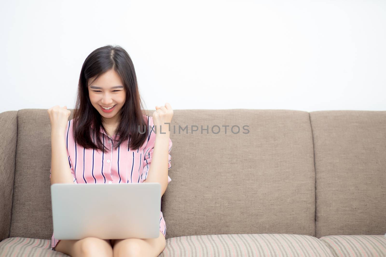 Beautiful of portrait asian young woman excited and glad of success with laptop on sofa, girl working living room at home, career freelance business concept.