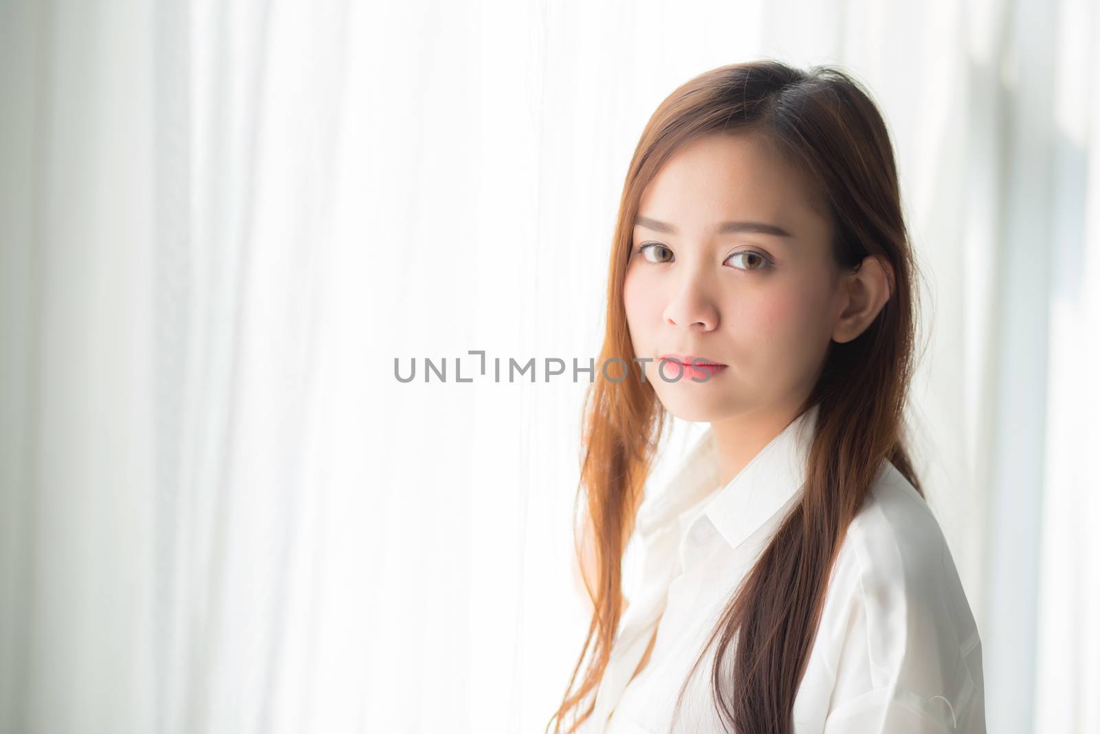 Portrait of beautiful young asian woman standing the window and smile while wake up with sunrise at morning, lifestyle and relax concept.