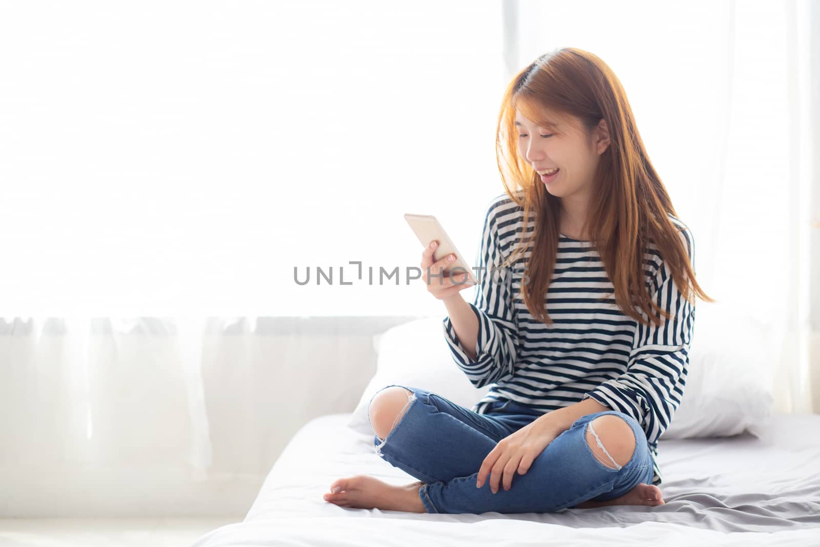 Beautiful young asian woman smiling sitting relax on the bed in the morning, girl using mobile smart phone talking enjoy, communication and social network concept.