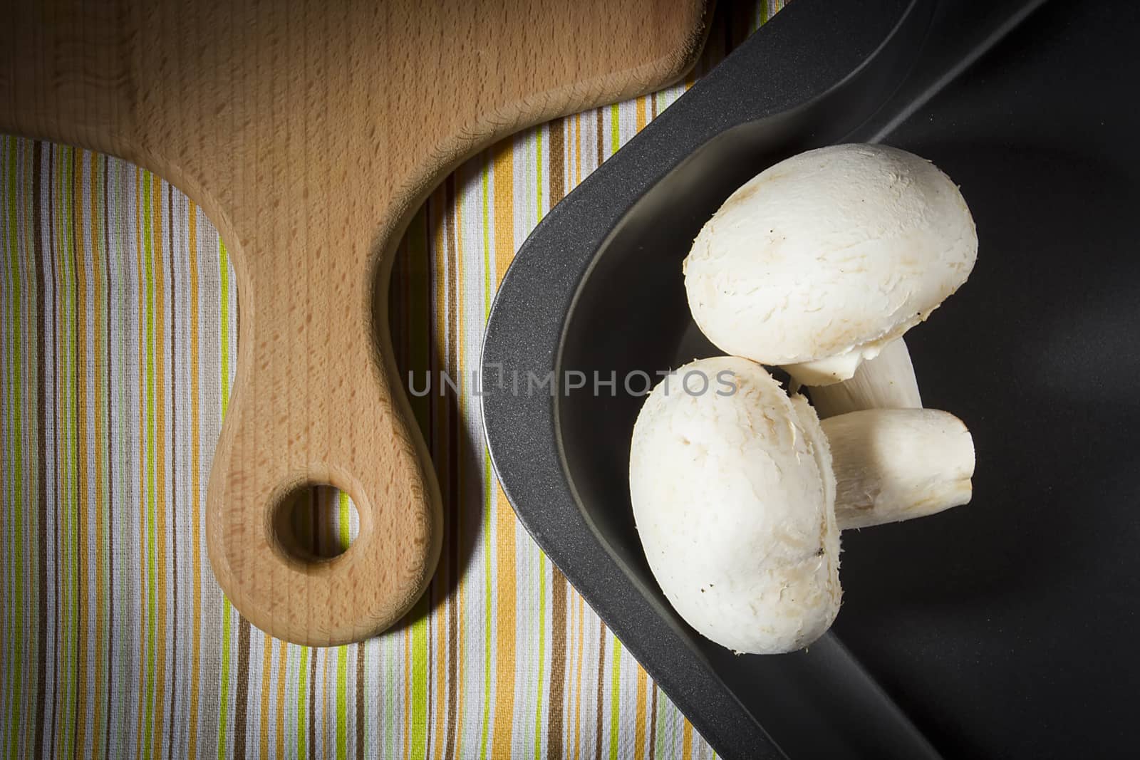 Champignon mushrooms on a baking sheet and a cutting board on the kitchen table