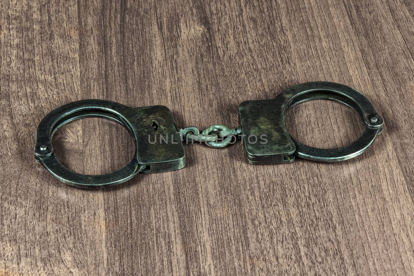 Metal handcuffs lie on a wooden table by Grommik