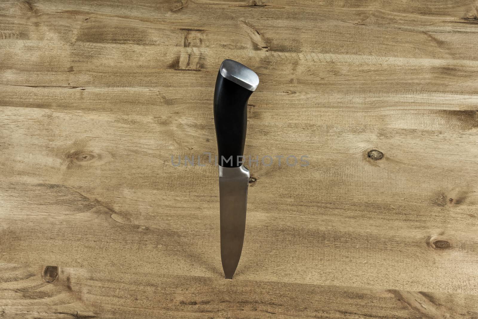 A metal knife with a black handle is stuck in a wooden stand