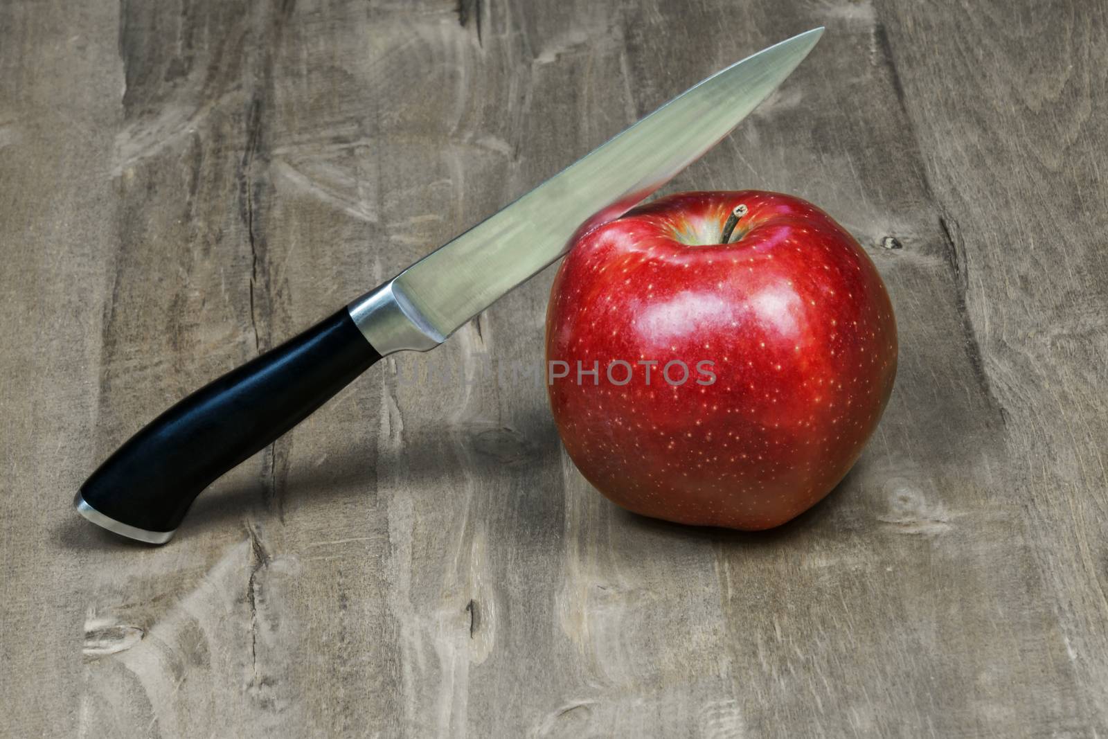 The knife cuts a red apple lying on a wooden surface