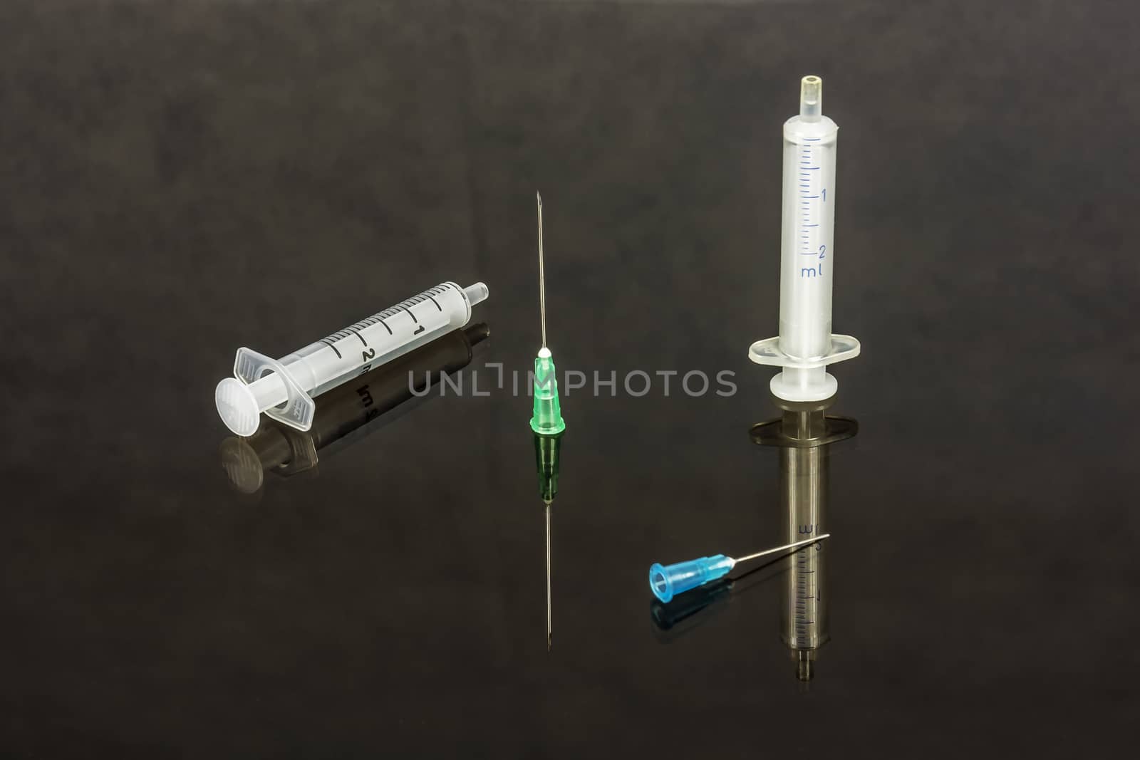Two medical syringes with needles lie on a glass surface by Grommik