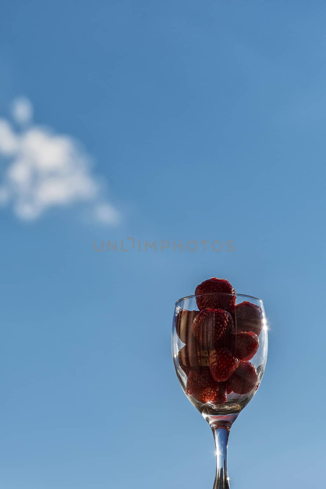 Strawberries in a glass against the blue sky by Grommik