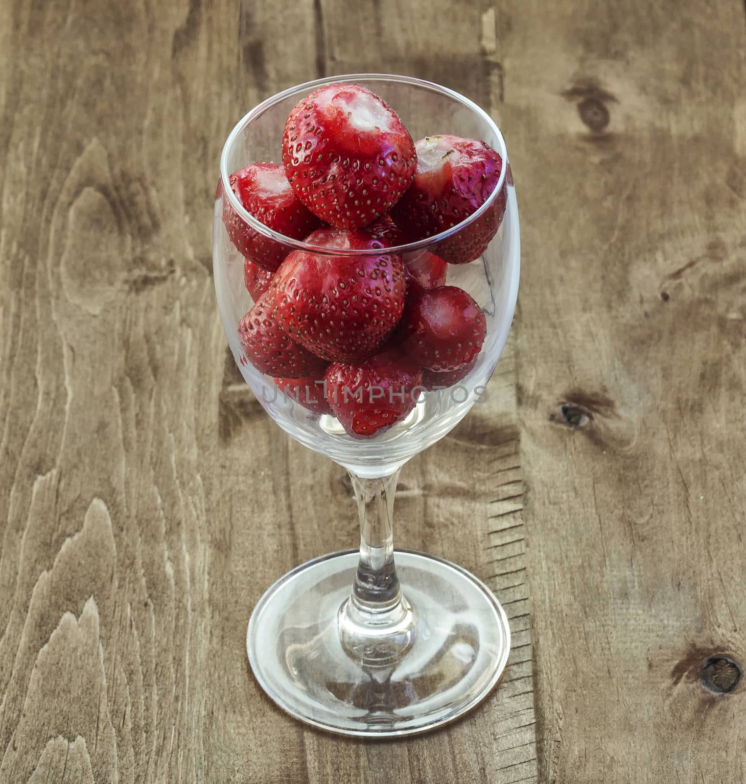 On the wooden surface is a glass wine glass with strawberries