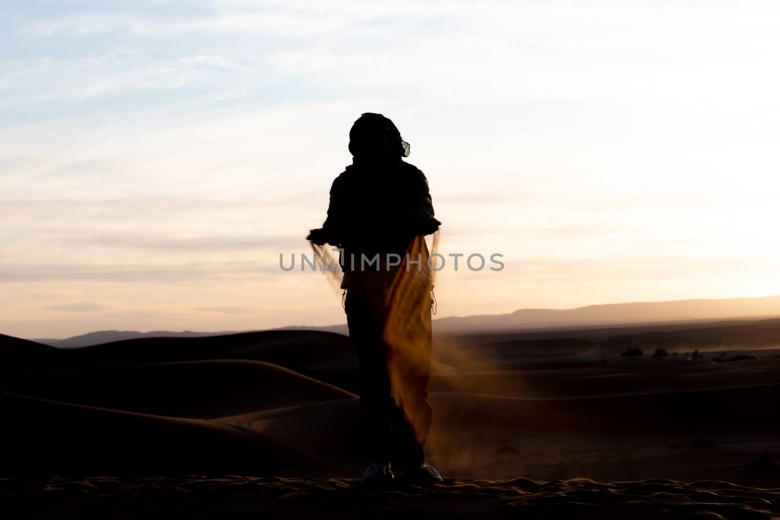 Silhouette of person jumping and throwing sand in the Sahara against a sunset. High quality photo