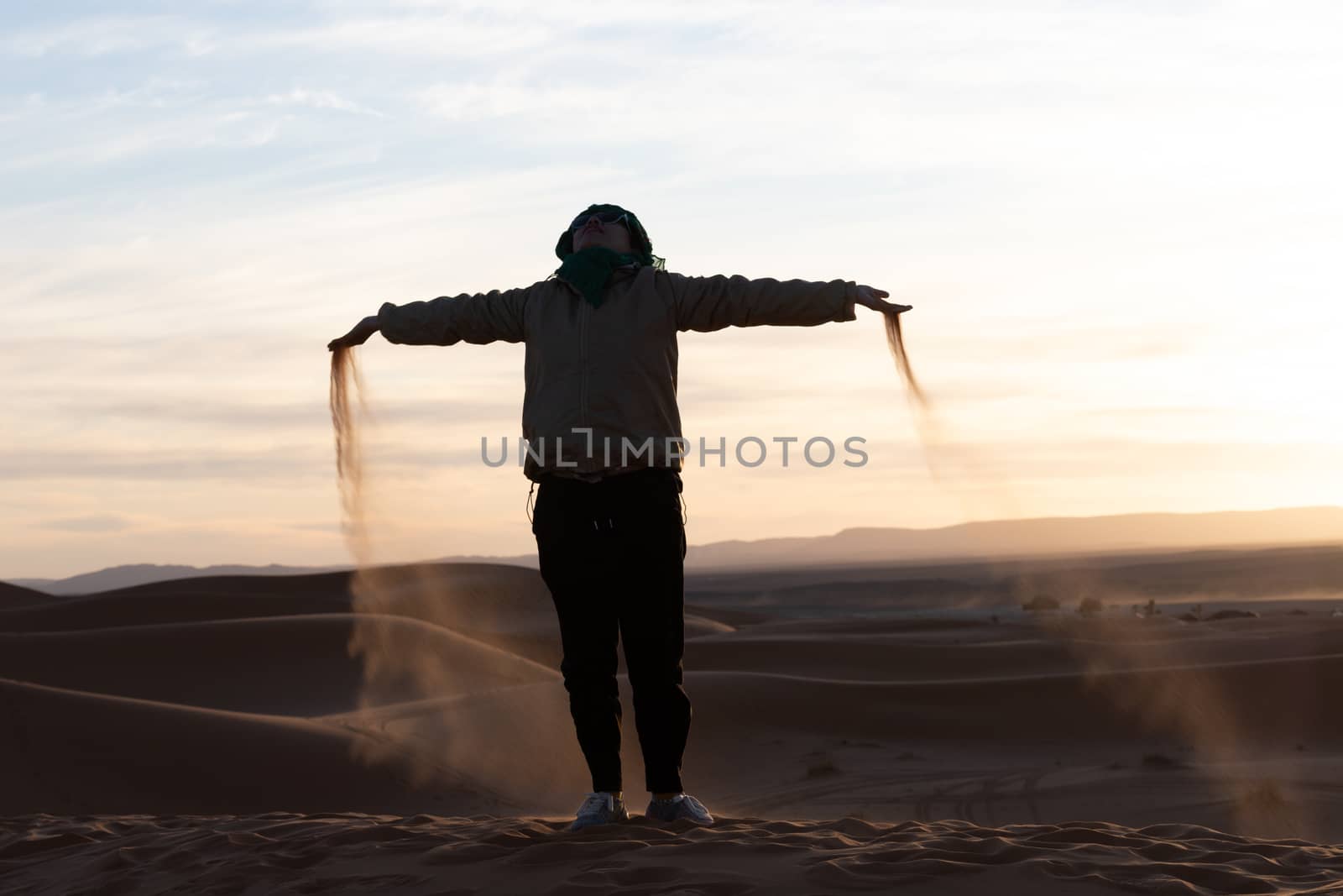 Silhouette of person jumping and throwing sand in the Sahara against a sunset by kgboxford
