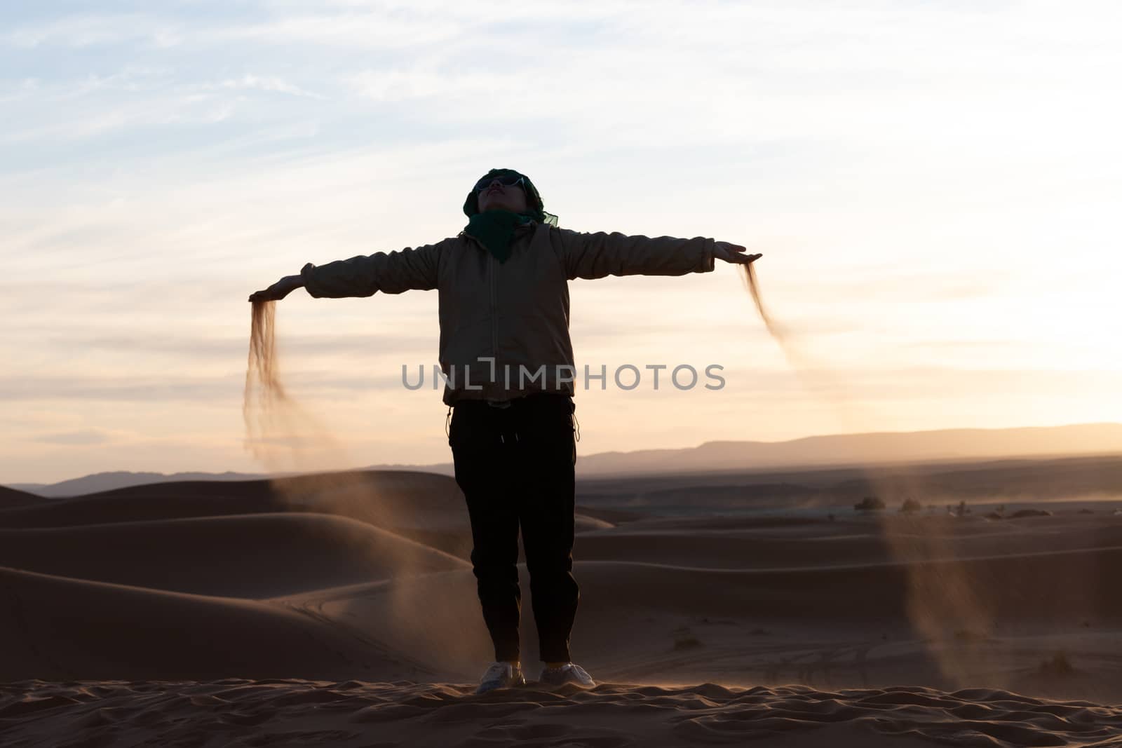 Silhouette of person jumping and throwing sand in the Sahara against a sunset. High quality photo