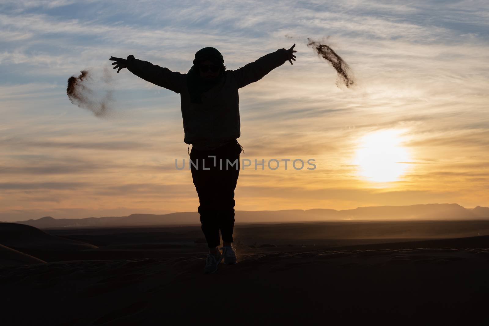 Silhouette of person jumping and throwing sand in the Sahara against a sunset by kgboxford