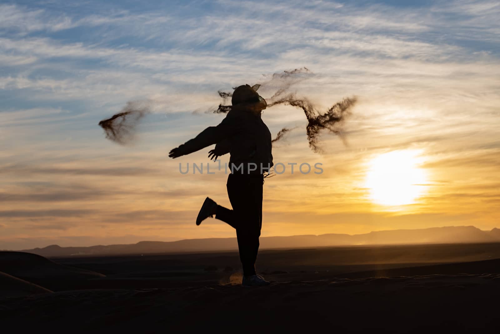 Silhouette of person jumping and throwing sand in the Sahara against a sunset. High quality photo