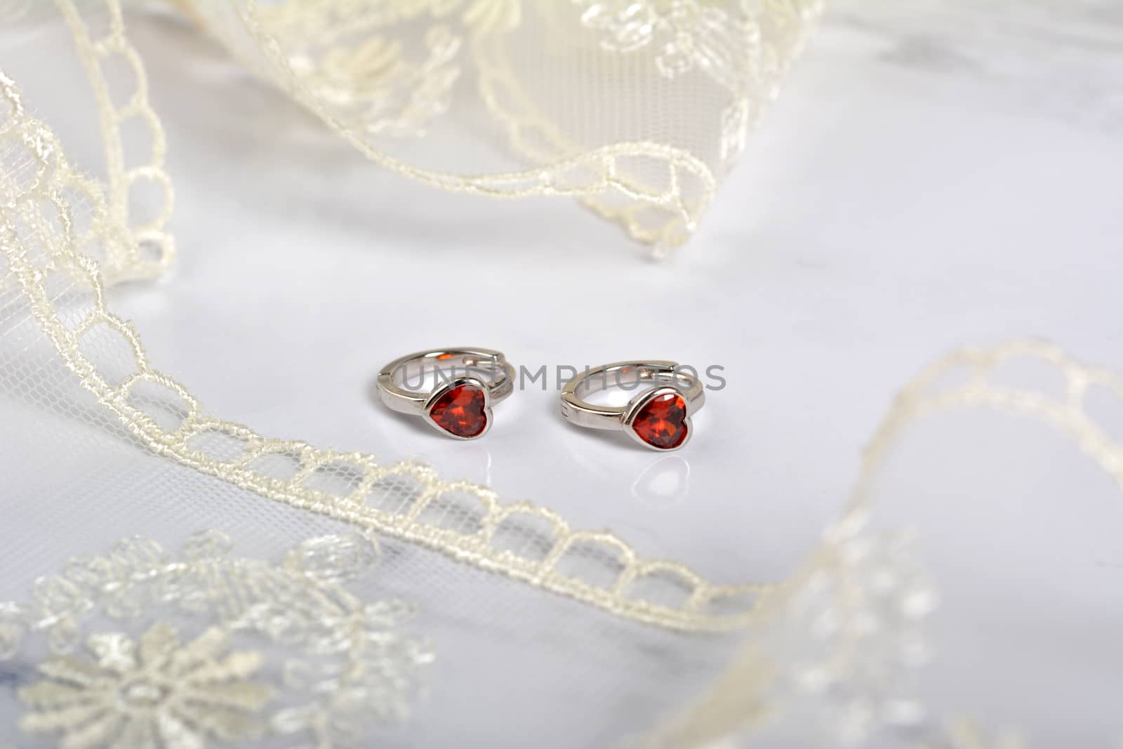 silver earrings with red glass hearts with delicate ecru lace on a light gray background. space for text. jewelry advertising texture