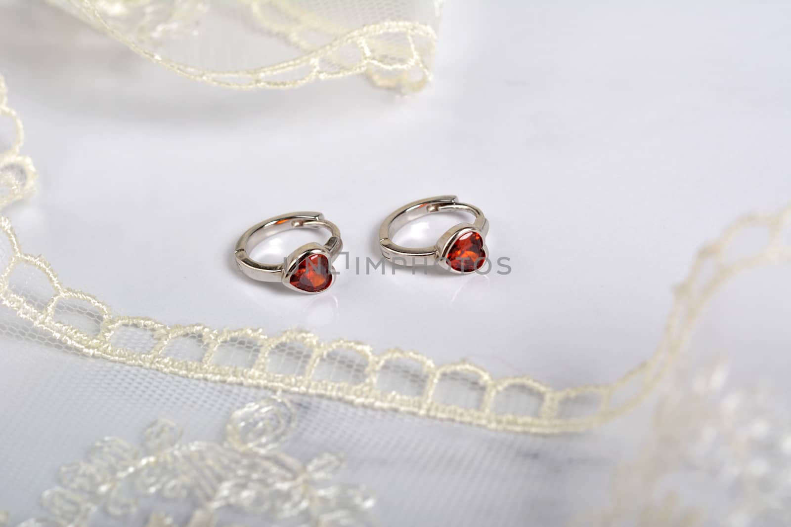 silver earrings with red glass hearts with delicate ecru lace on a light gray background. space for text. jewelry advertising texture