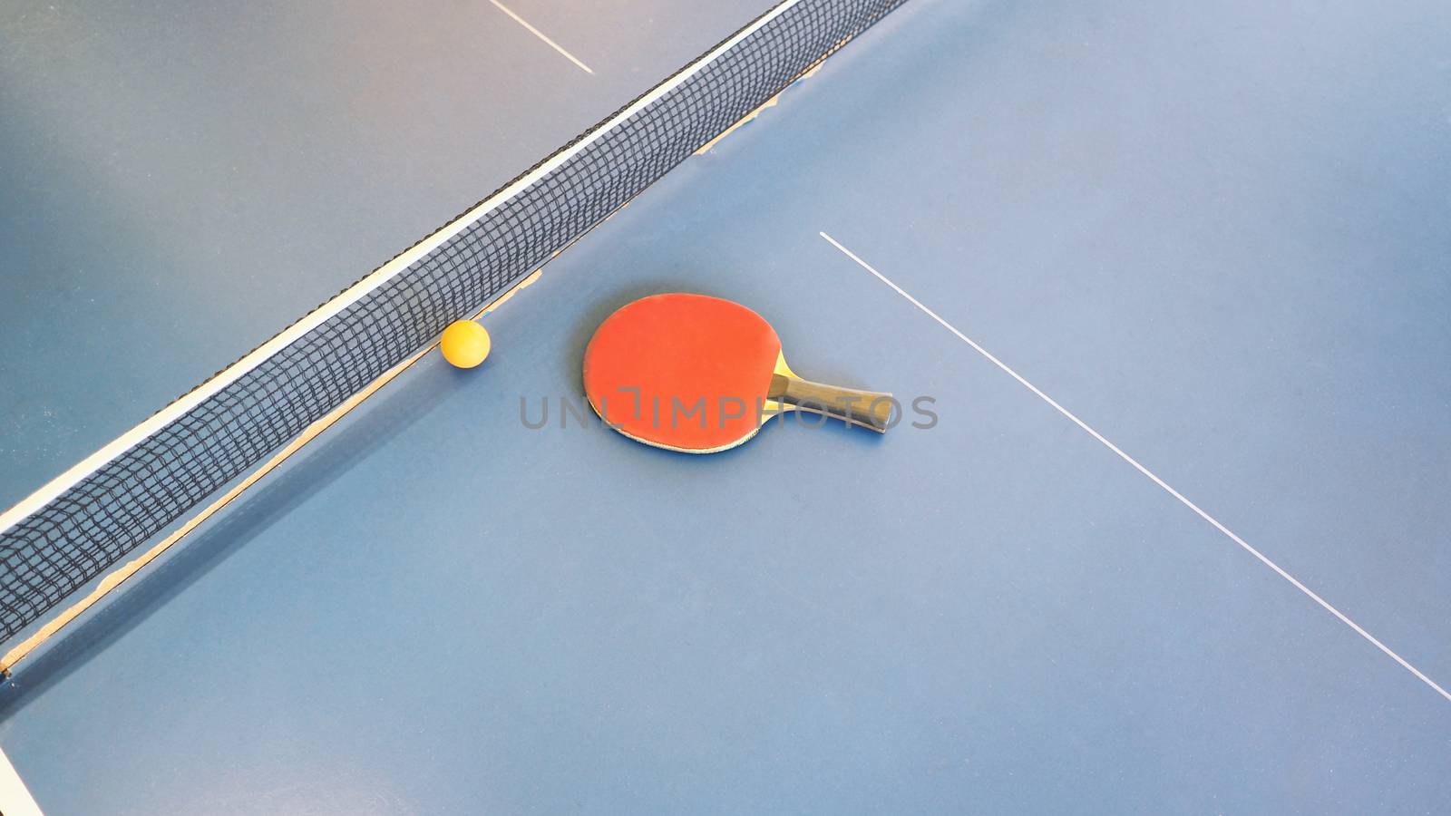 Top view of table tennis or ping-pong table with red and black color wood racket and yellow ball.