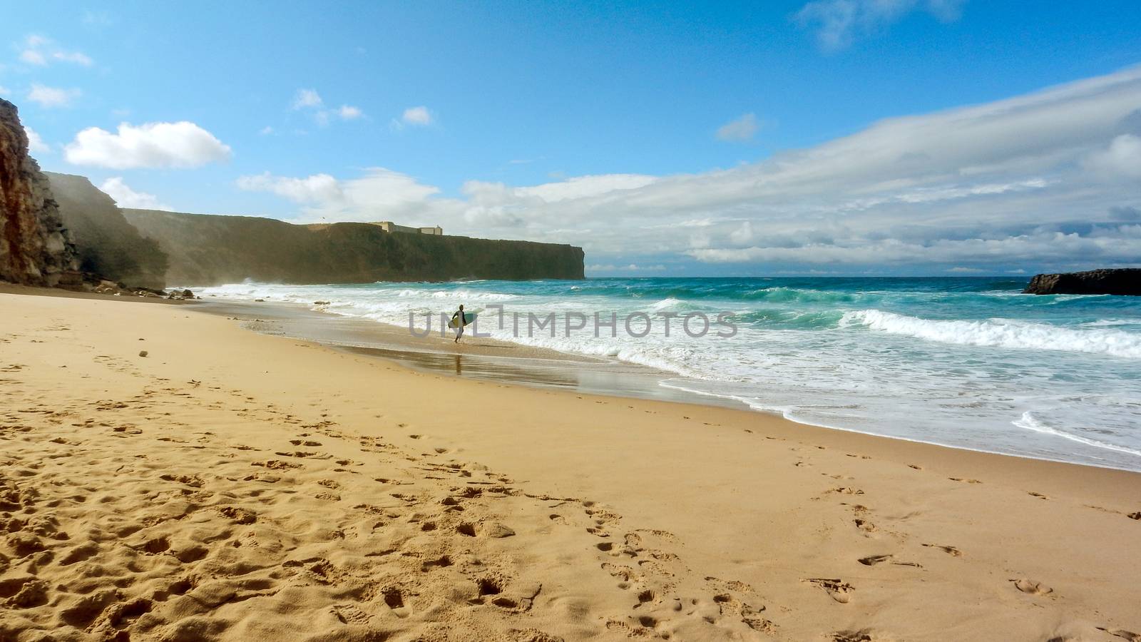 Lone surfer with the board under his arm is about to face the waves of the ocean in the Algarve, Portugal - Enjoy your freedom by practicing concept by robbyfontanesi
