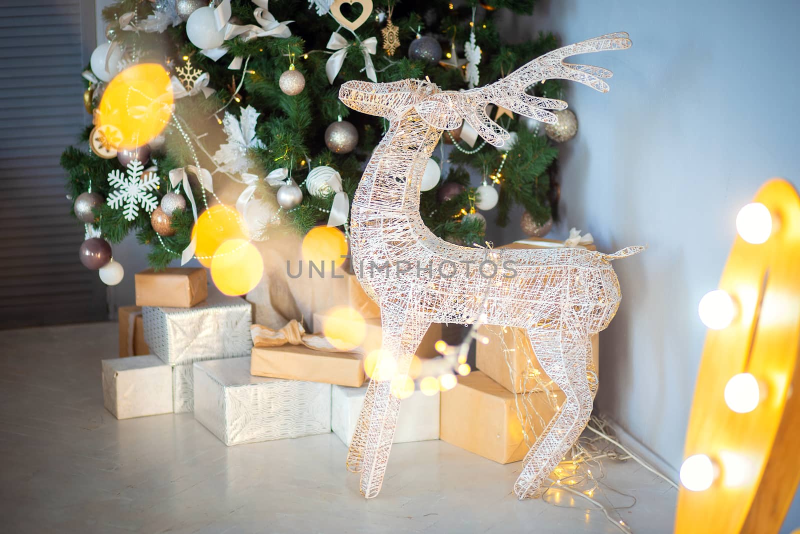 A festive decorative deer stands in the room against the background of a Christmas tree and a mountain of gifts. Gifts for the new year under the tree. Holiday atmosphere