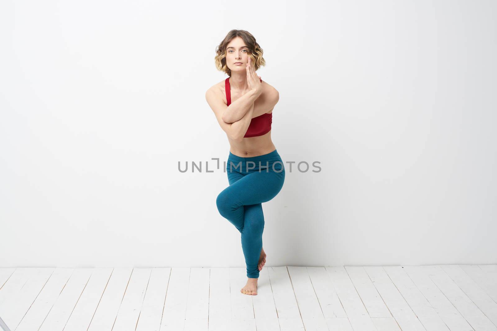 sports woman in a bright room doing yoga in full growth blue leggings and a red tank top. High quality photo